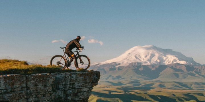 Cyclist on hill with snowy mountain might be in Europe