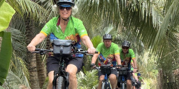 Female Cyclist leading single file under coconut palms